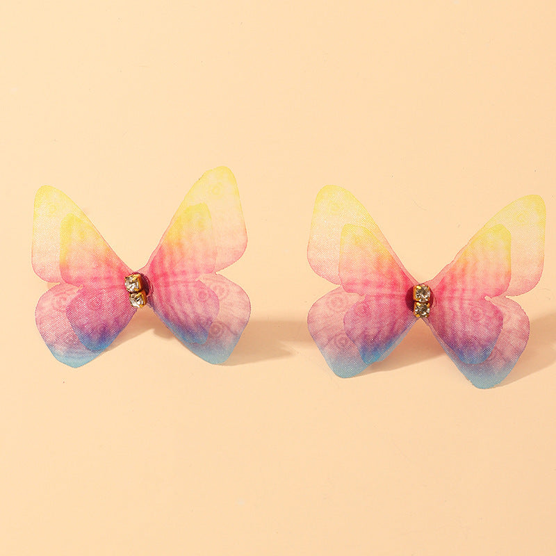 Butterfly-shaped earrings with pink and blue gradient on a beige background