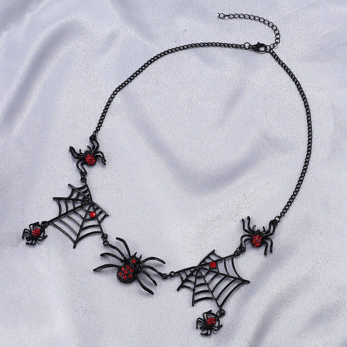 Gothic-style necklace with spider and web designs on a white fabric background