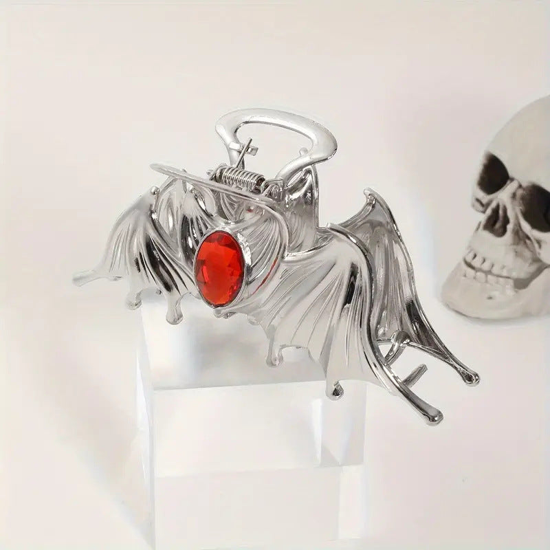 Metallic bat-shaped object with a red gemstone on a white background