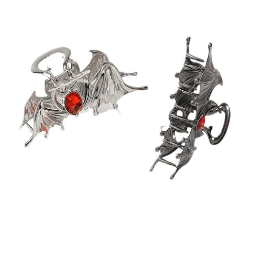 Two dragon-shaped brooches, one silver with red gem and the other black, on a white background.