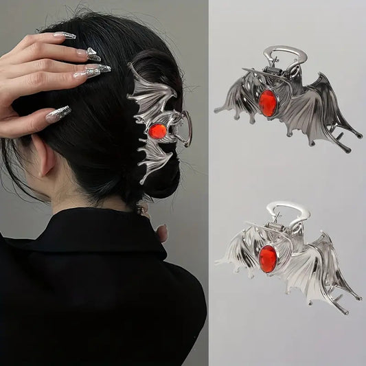 Bat-shaped hair clip with red gemstones worn by a person, with close-up details on a gray background.