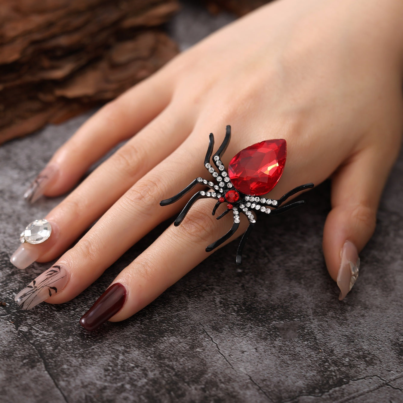 Hand wearing a red gemstone spider ring on a dark surface