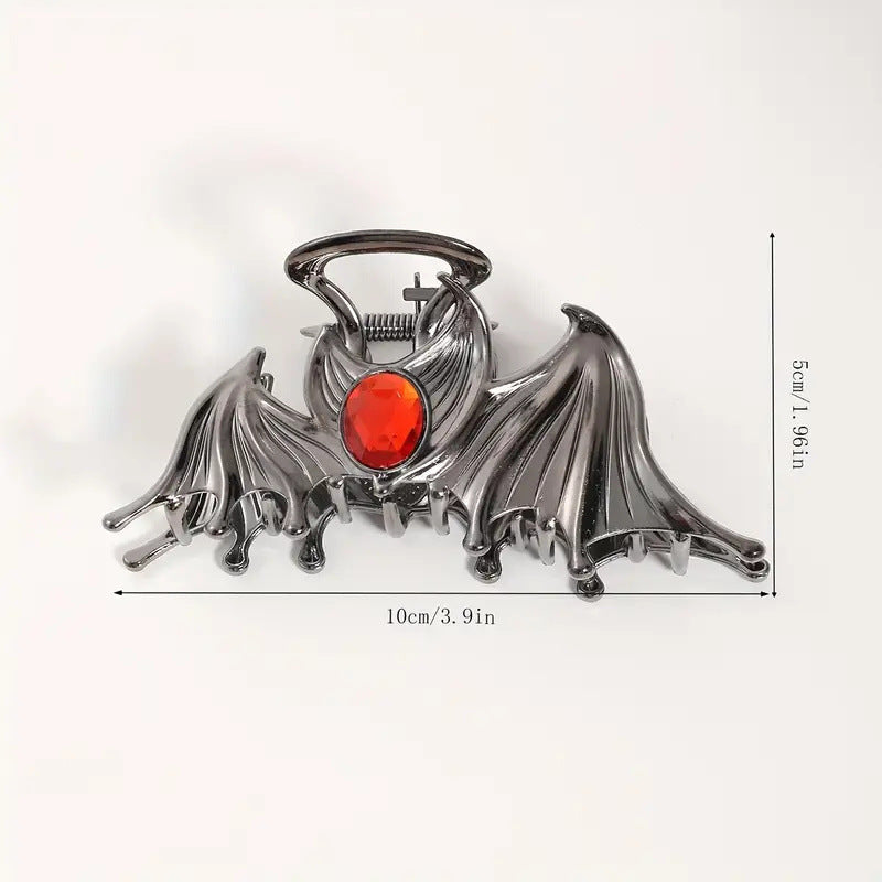 Metallic bat-shaped object with a red gemstone on a white background
