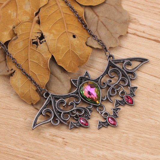 Ornate necklace with a teardrop-shaped gem and red stones on a wooden surface with leaves.