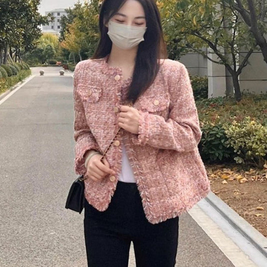 Woman wearing a pink textured jacket and black pants on a street.