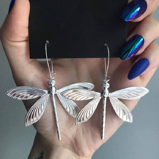 Silver dragonfly earrings held in a hand with blue nail polish.