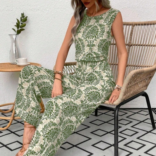 Woman sitting on a wicker chair wearing a green and white floral jumpsuit.