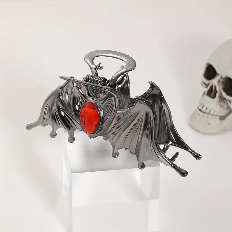 Metallic bat-shaped object with a red gem on a white background