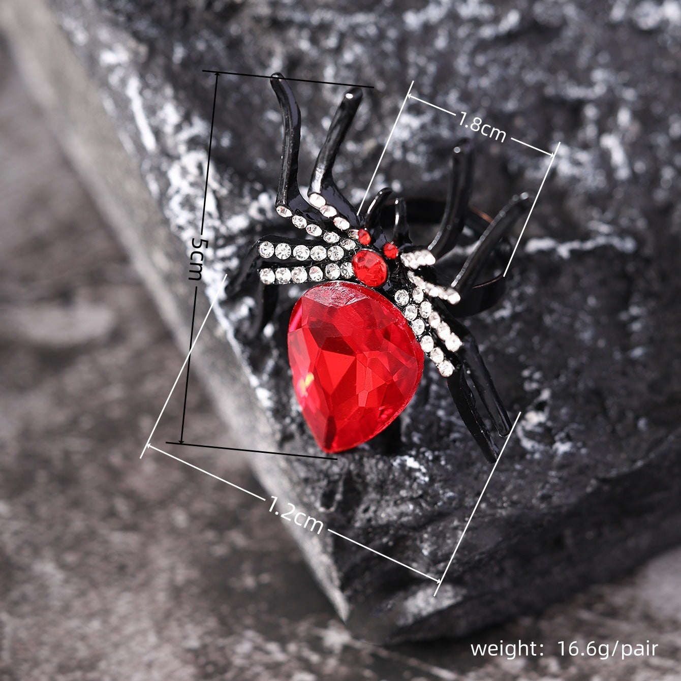 Black spider-shaped brooch with a red gemstone on a textured background