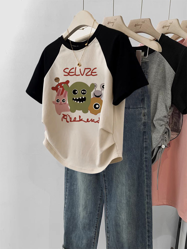 Black and beige t-shirt with cartoon designs and text on a hanger against a white wall.
