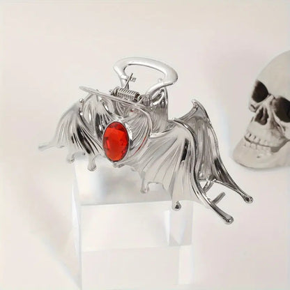 Metallic bat-shaped object with a red gemstone on a white background