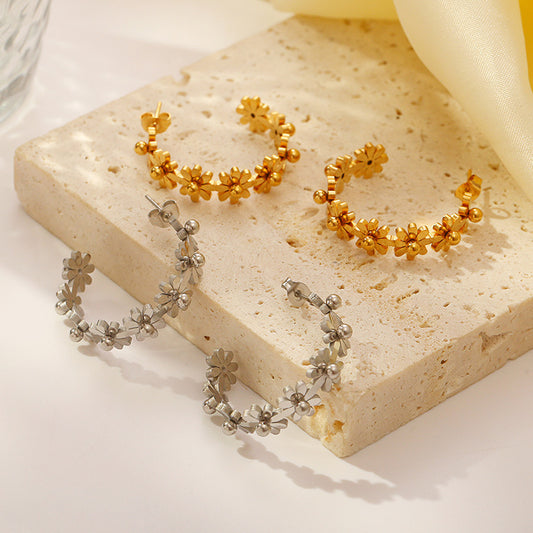 Gold and silver floral hoop earrings on a light stone surface.