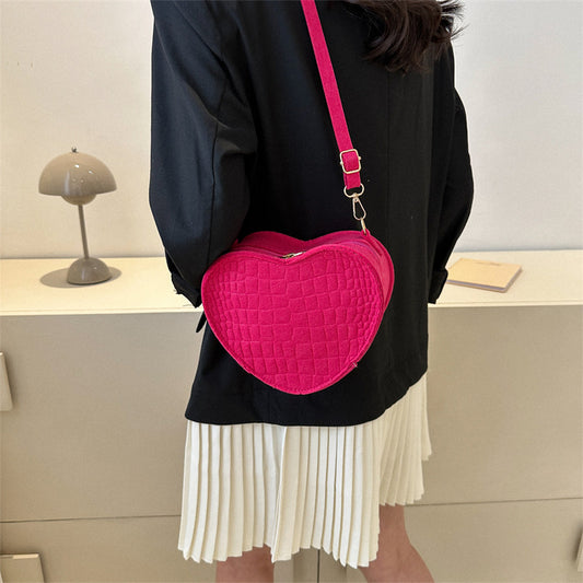 Person wearing a black top and white pleated skirt with a pink heart-shaped bag.